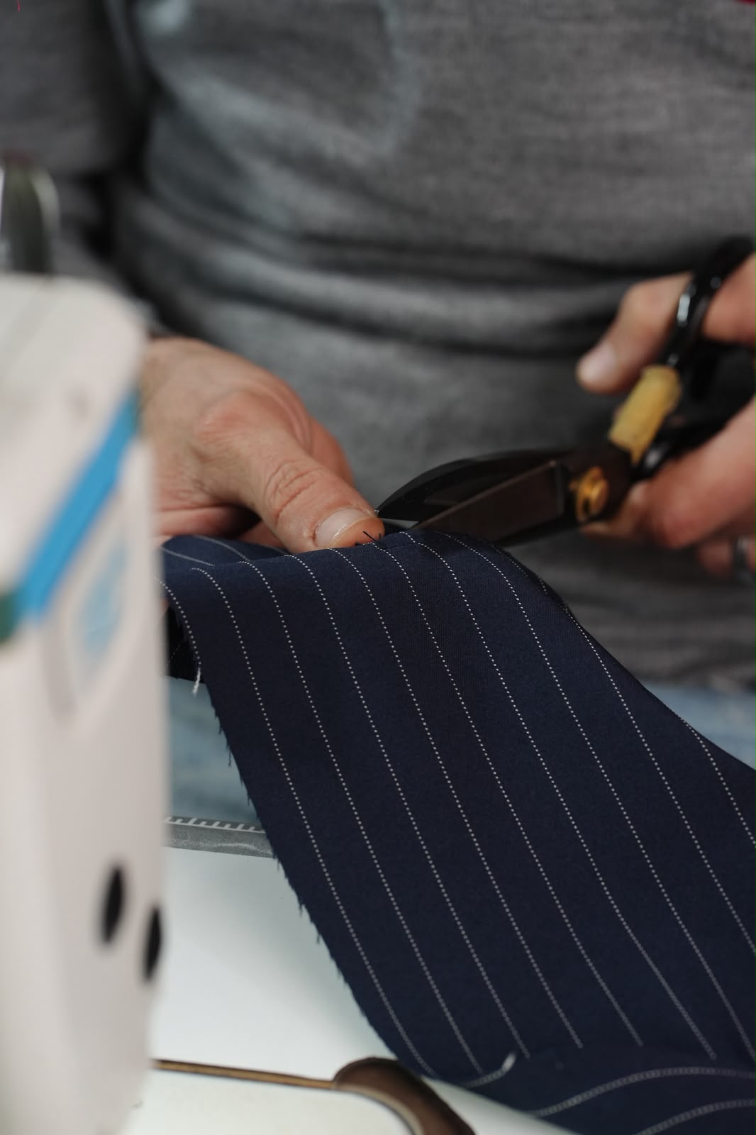 Hands cutting navy pinstripe cloth beside a sewing machine
